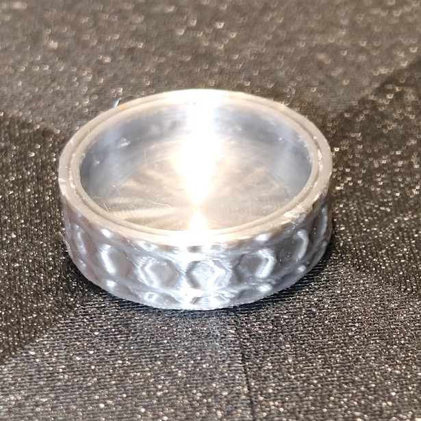 Silver ring with textured design on a dark textured surface